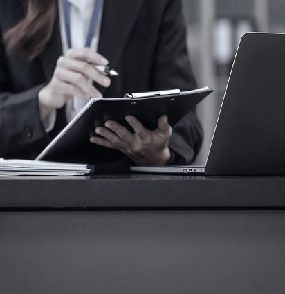 Businessperson signing documents at desk with laptop.